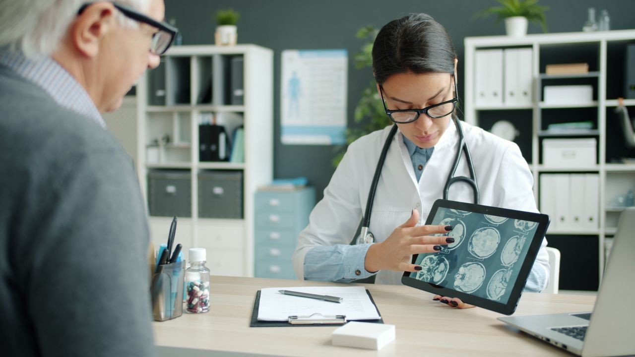 A doctor using a digital tablet to explain brain scans to a patient in a medical office.